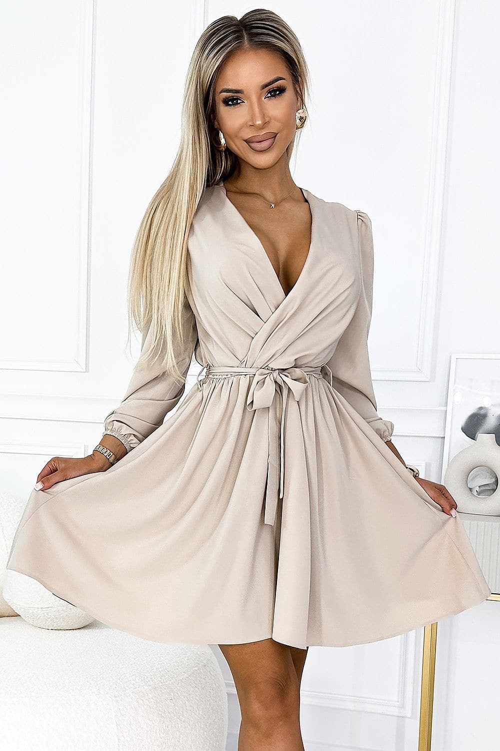 Robe de cocktail beige courte chic avec ceinture, manches longues et décolleté plongeant idéale pour événements et soirées élégantes.