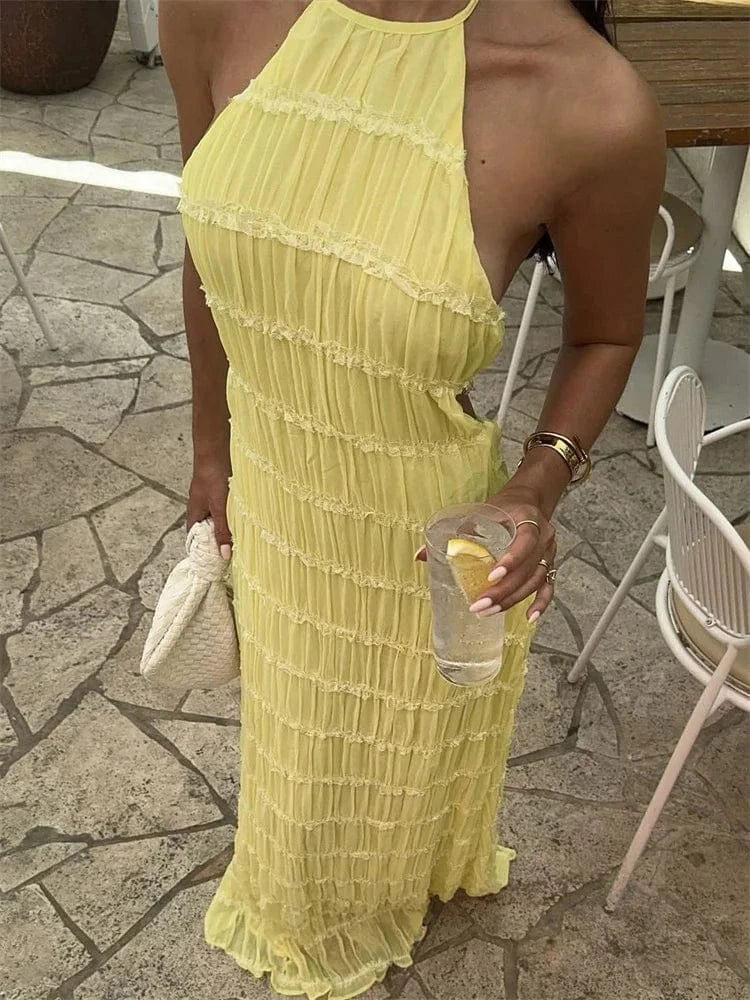 Robe longue évasée jaune été sans manches style bohème chic femme accessoirisée d’une pochette tressée blanche
