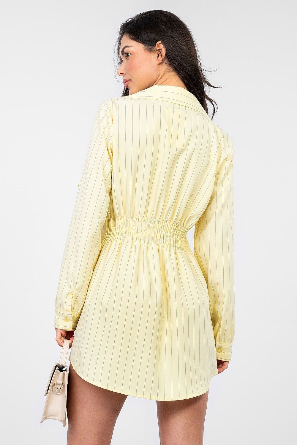 Robe chemise courte jaune à rayures manches longues, style casual été, accessoirisée d’un sac à main beige