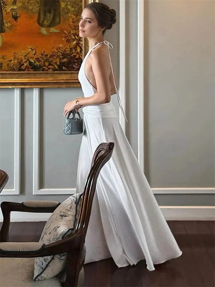 Robe de soirée mariage blanche longue dos nu fluide élégante invitée chic avec sac à main tendance