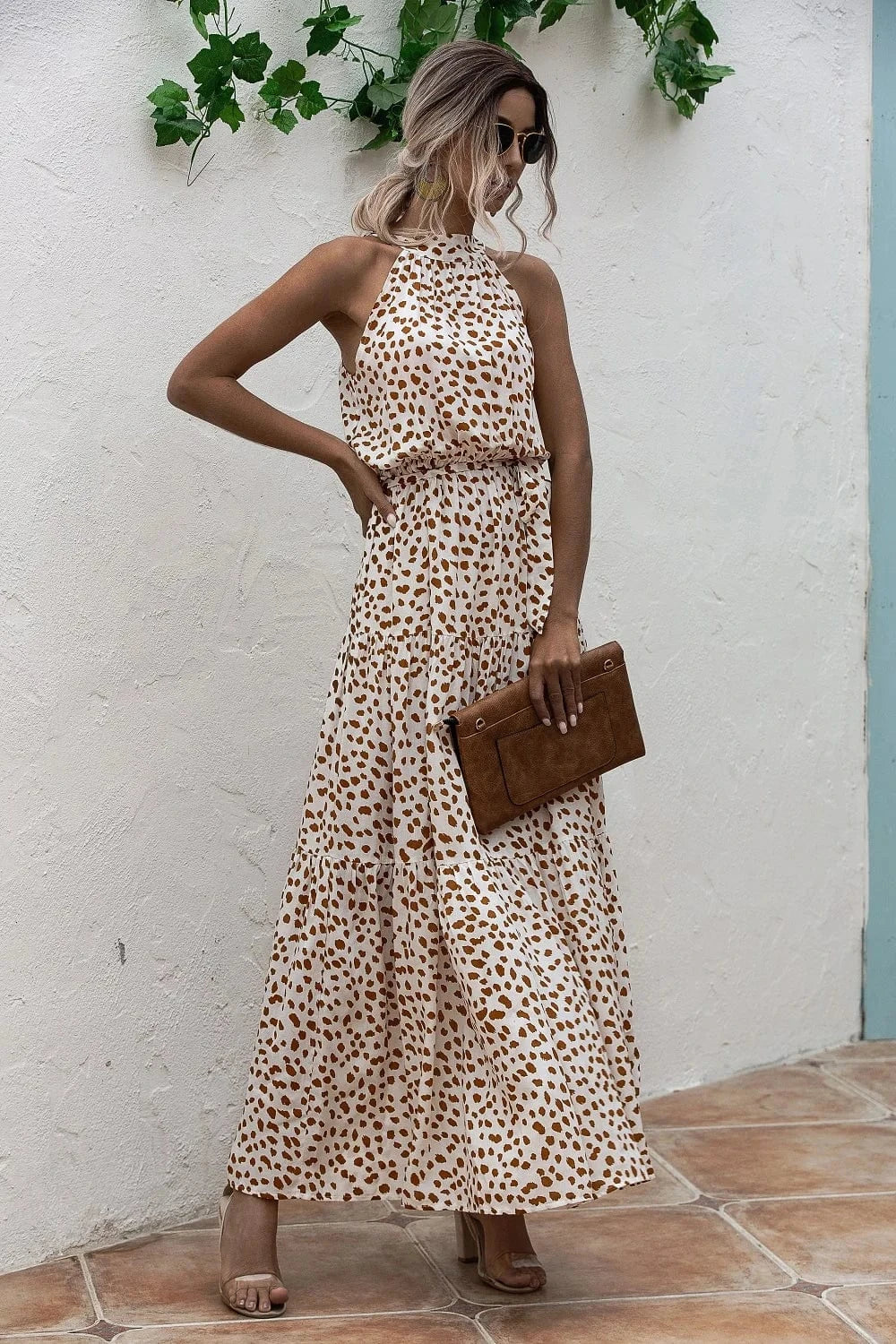 Robe longue été fluide bohème blanche à motifs marron sans manches, accessoirisée d’une pochette marron tendance